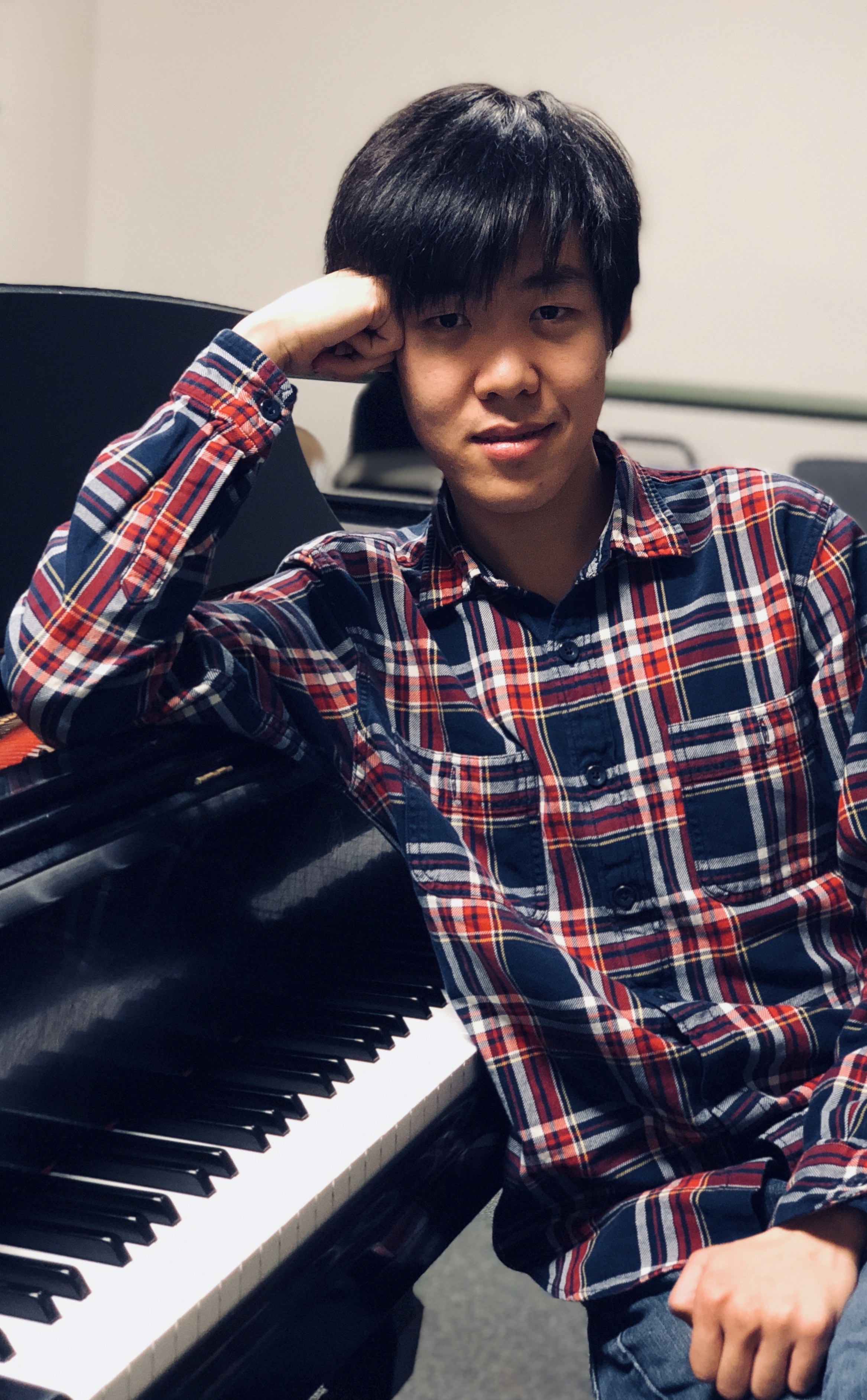 New England Conservatory's Yutong Sun sitting on a piano bench, leaning on a piano.