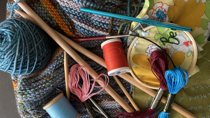 image of yarn, knitting needles, crochet hooks, spools of thread, embroidery thread and hoop, and knitting in progress. , and a  