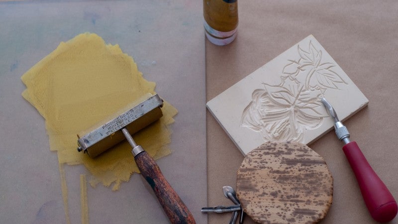plexi plate with gold ink next to carved printmaking block, baren, and linoleum cutter