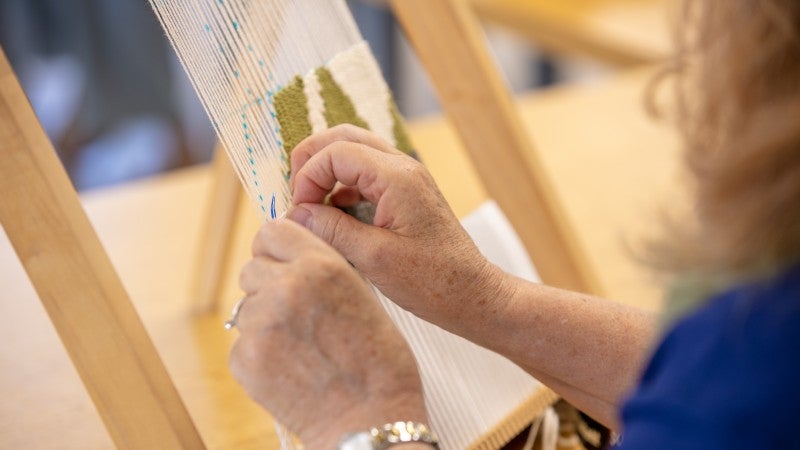person weaving yarn through warp thread on large loom