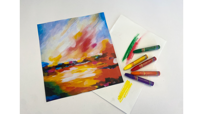 a fall landscape created with crayons and a set of colorful crayons displayed next to it