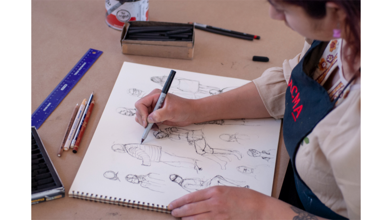 seated person drawing figures in sketchbook