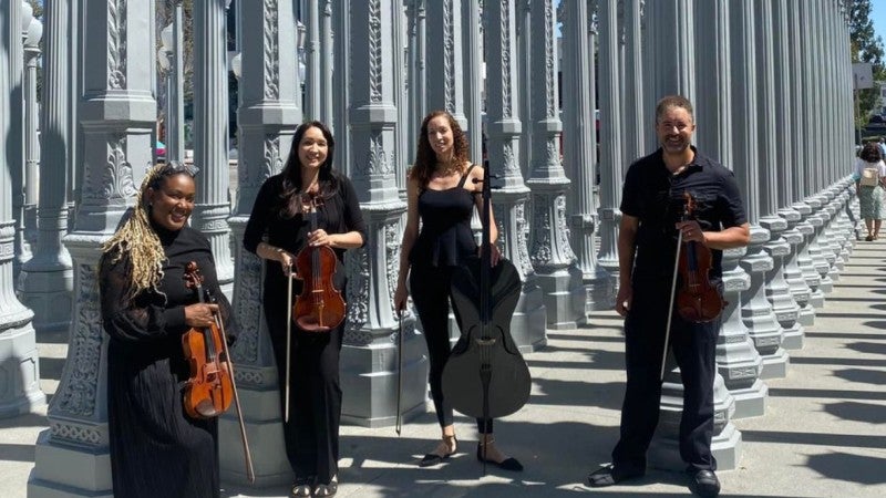 string quartet and their instruments standing in front of Chris Burden's Urban Light