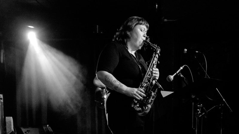 black and white still of Nicole McCabe performing on saxophone