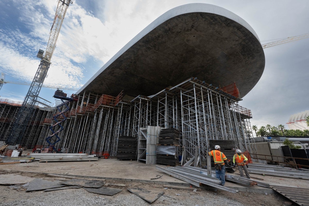 Curved gray building cantilevered over scaffolding on a construction site