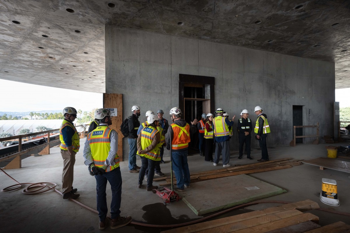 A large group of people in safety helmets and vests inside gray concrete building under construction